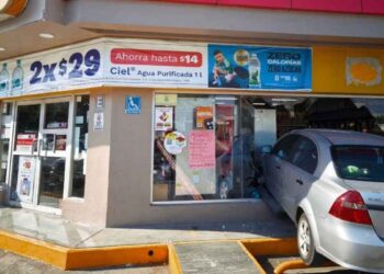 Automóvil gris Chevrolet Aveo incrustado en la fachada de una tienda de conveniencia